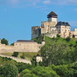 Trencin Castle perched on a hilltop surrounded by lush greenery under a clear blue sky in Trencin, Slovakia