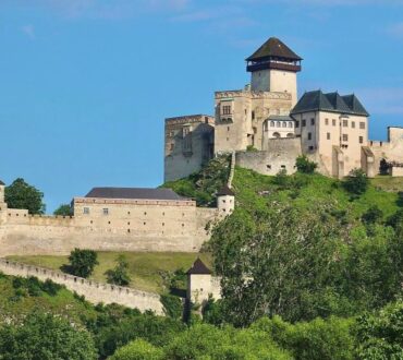 Trencin Castle perched on a hilltop surrounded by lush greenery under a clear blue sky in Trencin, Slovakia