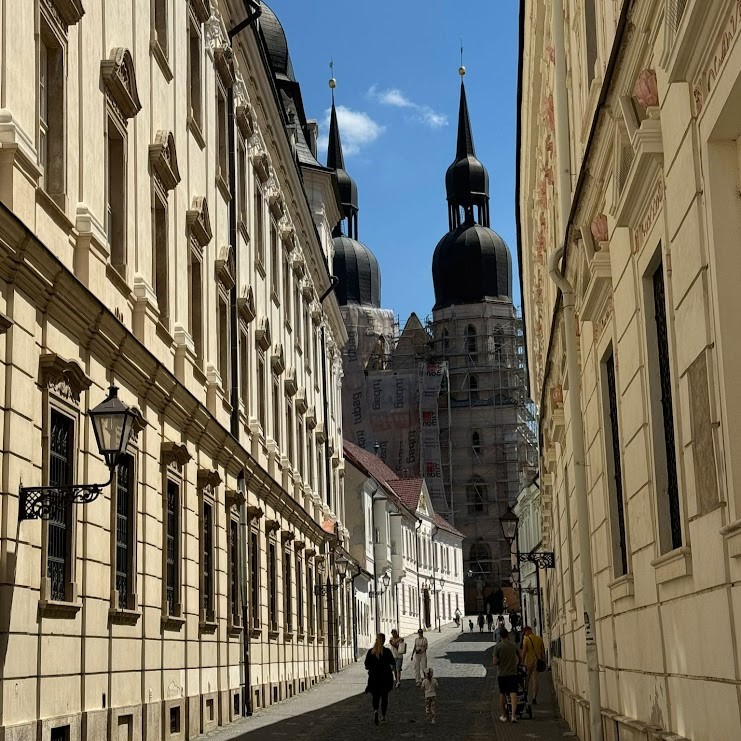 Historic street in Trnava, Slovakia, leading to the twin spires of St. John the Baptist Cathedral, with people walking on a sunny day during their day trip to Trnava