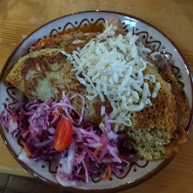 Salty pancake from potato filled with chicken . On the top the slices of cheese and cabbage with tomato served in traditional wooden restaurant of Slovakia called Koliba.